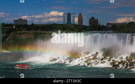 Le bateau de croisière Hornblower voyageant sous un arc-en-ciel devant les chutes américaines à Niagara Falls avec une ville de New York en arrière-plan. Banque D'Images