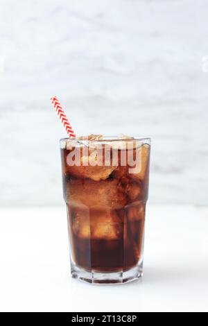 Cola glacé sur grand verre avec paille de papier à rayures rouges, sur fond blanc. Isolé Banque D'Images