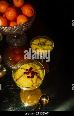 Sholeh Zard, un dessert de riz au safran persan recouvert de cannelle et de pistaches sur la table avec un bol de fruits d'oranges et de fond sombre Banque D'Images