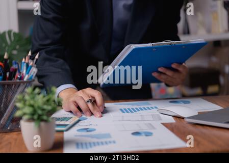 L'homme d'affaires vérifie l'analyse graphique de rapport de marketing avec l'ordinateur portable sur le bureau. Banque D'Images