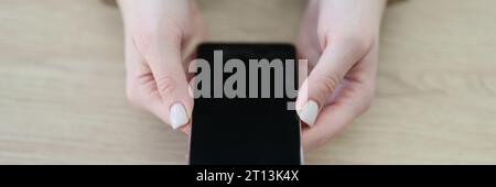 Une femme aux menottes tient un smartphone moderne assis à une table Banque D'Images