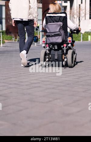 homme marchant avec une femme en fauteuil roulant électrique Banque D'Images