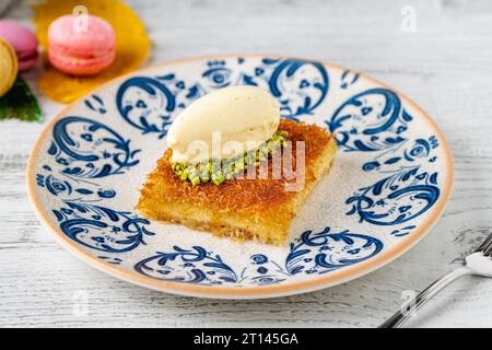 Kunefe avec des pistaches et de la crème glacée sur une assiette en porcelaine sur une table en bois Banque D'Images