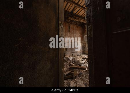 La porte en bois à moitié ouverte menant à la salle détruite par les intempéries d'un bâtiment abandonné à la lumière du jour Banque D'Images