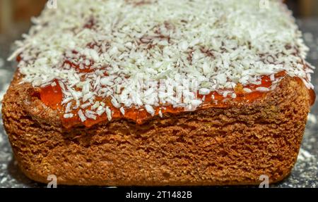 Un gâteau maison garni de confiture de fruits qui coule et de flocons de noix de coco. Banque D'Images