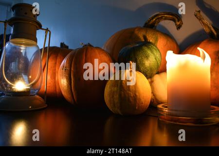 Une sélection de citrouilles et de courges affichées sur une table noire avec une bougie et une lanterne de tempête de lumière de thé projetant de la lumière et de l'ombre sur eux. Banque D'Images