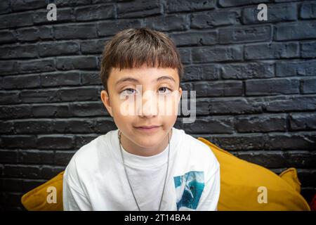 Portrait d'un garçon de 10 ans avec un mur de briques peint en noir derrière. Banque D'Images