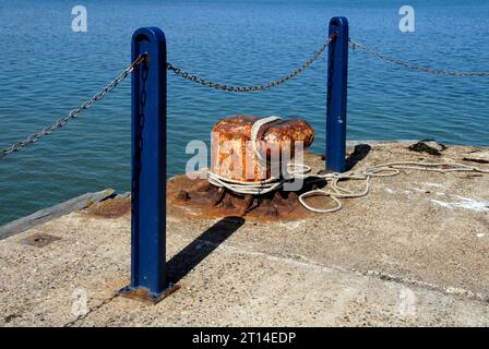 Grande borne avec corde autour et deux poteaux métalliques bleus au bout de la jetée en béton, Whitstable, Kent Banque D'Images