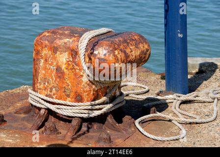 Grand bollard avec corde autour et une partie de poteau métallique bleu à l'extrémité de la jetée en béton, Whitstable, Kent Banque D'Images