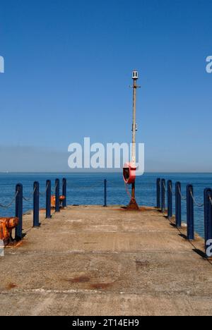 Jetée en béton avec bornes et poteaux métalliques bleus au bord et bouée de sauvetage au bout, Whitstable, Kent Banque D'Images