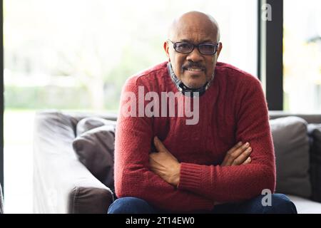 Portrait de l'homme biracial senior heureux portant des lunettes assis sur le canapé à la maison Banque D'Images