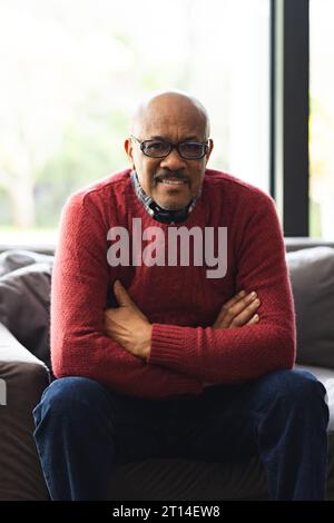 Portrait de l'homme biracial senior heureux portant des lunettes assis sur le canapé à la maison Banque D'Images