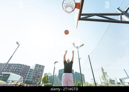 Concept de sports, de loisirs et de mode de vie sain. Jeune fille athlétique s'entraîne pour jouer au basket-ball sur un terrain de basket-ball extérieur moderne. Femme heureuse Banque D'Images