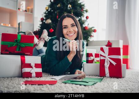 Photo de femme drôle pensive habillée tricotée x-mas pull écriture invitations cartes postales à l'intérieur de la maison chambre Banque D'Images