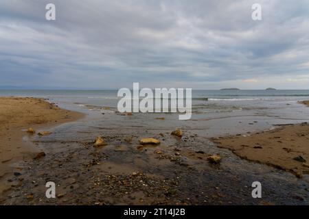 À marée basse, l'eau d'un petit ruisseau descend la plage de Llanbedrog et pénètre dans la mer. Banque D'Images