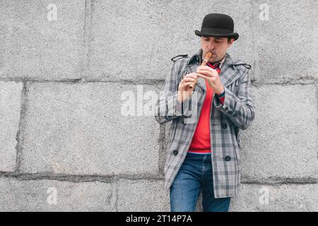 Style de vie urbain. Musicien de rue jouant d'un instrument en bois sopilka sur le fond d'un mur gris Banque D'Images