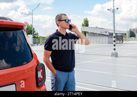 Jeune homme parle au téléphone dans la rue de la ville près de la voiture. Banque D'Images