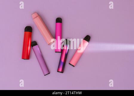 Cigarettes électroniques jetables colorées sur un fond violet. Le concept de tabagisme moderne, vapotage et nicotine. Vue de dessus Banque D'Images