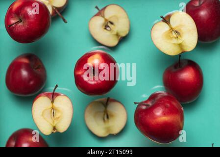 Des pommes entières et demi rouges flottent sur un fond bleu clair Banque D'Images