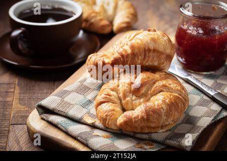 Deux croissants avec des conserves de fraises et une tasse de café sur une table en bois rustique Banque D'Images