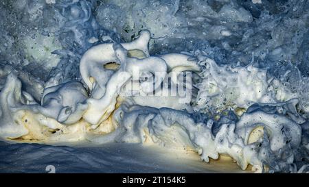 Gros plan photo de bulles de mousse éclaboussant alors que les vagues se brisent sur les rochers Banque D'Images