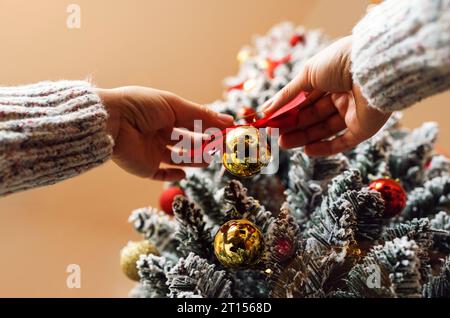 Boule d'or et ruban rouge décoration d'arbre de Noël dans les mains des femmes gros plan. Décorer le sapin de Noël. Banque D'Images