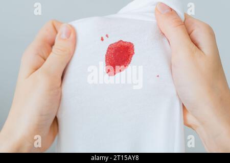 Déposez une tache de sang sur un chiffon blanc. Les mains des femmes tiennent les vêtements souillés et inspectent. Tache sale pour le concept de nettoyage Banque D'Images