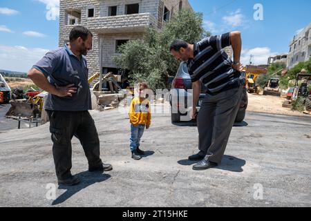 Bayt Surik, Palestine – 19 juin 2023 : heureux entrepreneurs arabes debout avec un jeune garçon souriant en chemise jaune par une Maison en pierre blanche Banque D'Images