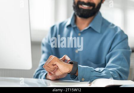 Homme d'affaires indien touchant la montre intelligente et la regardant, vérifiant le temps, en utilisant le gadget moderne dans le bureau, gros plan Banque D'Images