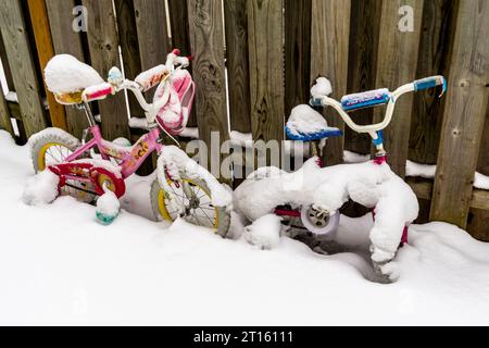 26 janvier 2023, Toronto, Canada - deux vélos jouets pour enfants couverts de neige contre une clôture en bois dans la cour arrière après une chute de neige. Banque D'Images