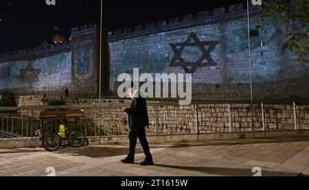 Vieille ville de Jérusalem, Israël. 11 octobre 2023. Un homme orthodoxe marche près des drapeaux israéliens projetés sur le mur de la vieille ville de Jérusalem après qu’Israël ait subi une attaque terroriste massive du Hamas à la frontière de Gaza, le mercredi 11 octobre 2023. Photo de Debbie Hill/ crédit : UPI/Alamy Live News Banque D'Images