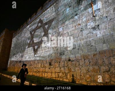 Vieille ville de Jérusalem, Israël. 11 octobre 2023. Un homme ultra-orthodoxe marche sous un drapeau israélien projeté sur le mur de la vieille ville de Jérusalem après qu’Israël ait subi une attaque terroriste massive du Hamas à la frontière de Gaza, le mercredi 11 octobre 2023. Photo de Debbie Hill/ crédit : UPI/Alamy Live News Banque D'Images