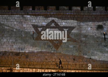 Vieille ville de Jérusalem, Israël. 11 octobre 2023. Un homme orthodoxe marche sous un drapeau israélien projeté sur le mur de la vieille ville de Jérusalem après qu’Israël ait subi une attaque terroriste massive du Hamas à la frontière de Gaza, le mercredi 11 octobre 2023. Photo de Debbie Hill/ crédit : UPI/Alamy Live News Banque D'Images