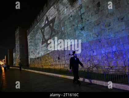 Vieille ville de Jérusalem, Israël. 11 octobre 2023. Un homme ultra-orthodoxe marche sous un drapeau israélien projeté sur le mur de la vieille ville de Jérusalem après qu’Israël ait subi une attaque terroriste massive du Hamas à la frontière de Gaza, le mercredi 11 octobre 2023. Photo de Debbie Hill/ crédit : UPI/Alamy Live News Banque D'Images