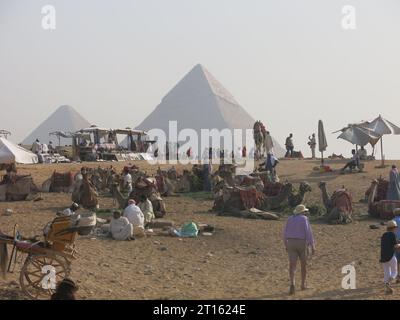 Tourisme aux Pyramides de Gizeh en Egypte : tôt le matin et les touristes se rassemblent au milieu des chameaux, des charrettes et des commerçants au pied de la Grande Pyramide. Banque D'Images