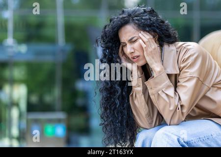 Femme adulte mature déprimée et avec mal de tête assise sur le banc à l'extérieur de l'immeuble de bureaux, surchargée et surchargée femme d'affaires triste, après le travail. Banque D'Images