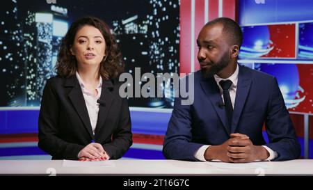 Équipe de journalistes divers sur talk-show la nuit, organisant un panel de divertissement pour discuter des dernières nouvelles de célébrités ou scandales. Homme et femme animent l'émission de nuit en direct sur le réseau de télévision. Banque D'Images