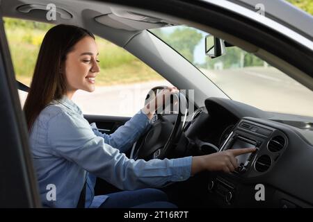 Sélection de la radio favorite. Belle jeune femme appuyant sur le bouton sur l'audio du véhicule dans la voiture Banque D'Images