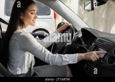 Sélection de la radio favorite. Belle jeune femme appuyant sur le bouton sur l'audio du véhicule dans la voiture Banque D'Images