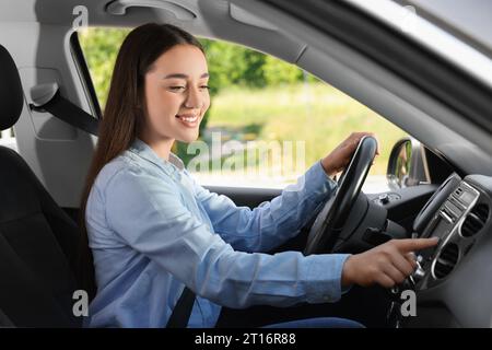 Sélection de la radio favorite. Belle jeune femme appuyant sur le bouton sur l'audio du véhicule dans la voiture Banque D'Images