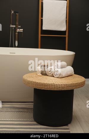 Journée spa. Serviettes et bougies sur une table en osier près de la baignoire dans la salle de bains Banque D'Images