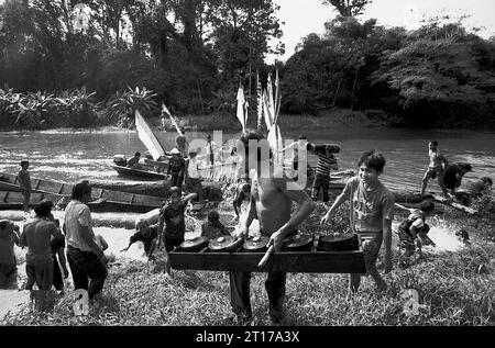 Kalimantan occidental, Indonésie. Mars 2007. Un homme décharge un jeu d'instrument de percussion gamelan, alors qu'il passe devant une foule de gens - la communauté Dayak Tamambaloh - qui s'éclaboussent de l'eau les uns sur les autres comme un acte purifiant, devant un bateau qui vient de transporter la famille de leur nouveau chef traditionnel pour une visite au lieu de sépulture de leur ancien chef dans le village de Sungai Uluk Palin (Sungulo Palin), Putusibau Utara, Kapuas Hulu, West Kalimantan, Indonésie. La culture est un élément indispensable de tout développement, selon l ' Organisation des Nations Unies. Banque D'Images