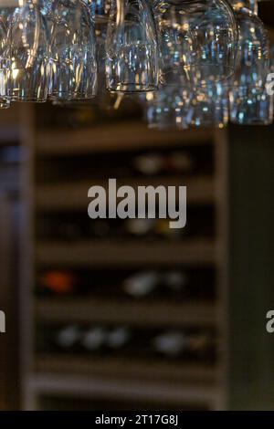 Nettoyez les verres à vin suspendus au-dessus du comptoir du bar sur fond flou avec une étagère avec des bouteilles de vin Banque D'Images