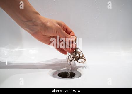 Tire à la main les cheveux hors de l'égout de la salle de bain. Système d'égouts pollués pour douche de nettoyage. Banque D'Images