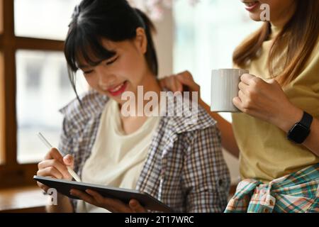 Heureuse femme asiatique utilisant la tablette numérique, partageant des idées ou de nouvelles informations à son collègue Banque D'Images