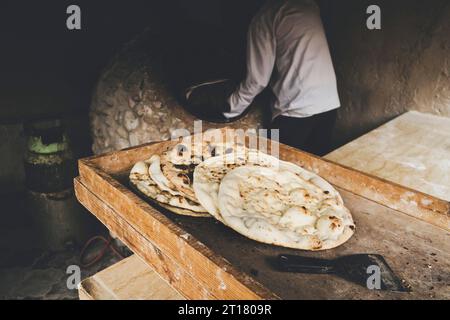 un homme âgé fait du pain traditionnel dans un vieux four rond en pierre dans un village rural. Cuisine d'Asie centrale. Pain chaud. Banque D'Images