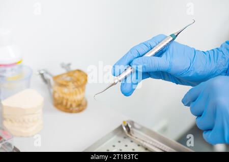 Les mains d'un dentiste tenant des instruments dentaires pour le traitement des dents, avec des modèles de mâchoires en arrière-plan. Banque D'Images