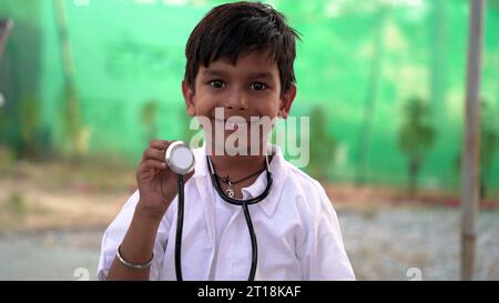 Mignon petit garçon indien porter un uniforme médical tenant stéthoscope jouant le médecin, heureux drôle petit enfant d'âge préscolaire de race mixte prétendant pediatrici Banque D'Images