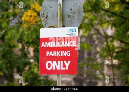 Stationnement ambulance SEULEMENT le panneau rouge NHS sur le poteau avec des branches d'arbre floues en arrière-plan Banque D'Images