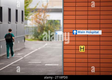 Vert uniforme homme / médecin / professionnel de la santé ou consultant entrant dans l'hôpital principal et marchant devant le signe à l'hôpital Exeter R D & E. Banque D'Images